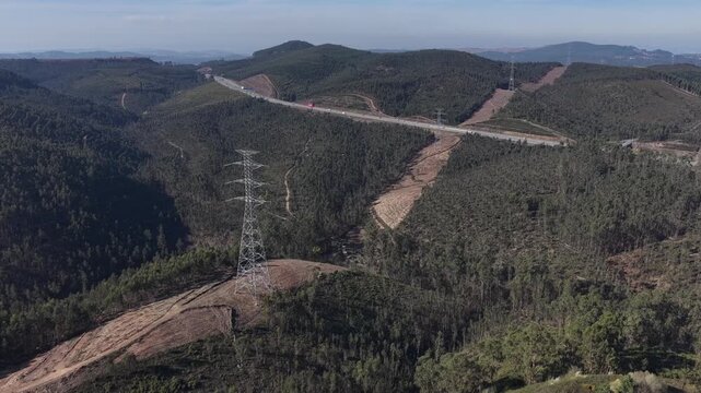 Aerial view of a highway cutting through a dense forest, contrasting with the stark lines of power lines and clear-cut paths, Valongo, Portugal.