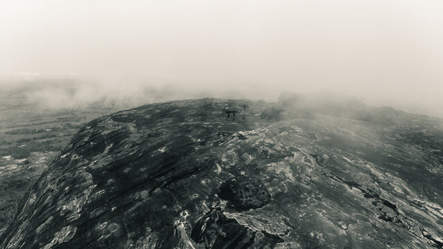 Aerial view of a rugged, rocky landscape shrouded in mist, revealing stark textures and tones under an ethereal sky, Oyo, Oyo, Nigeria.