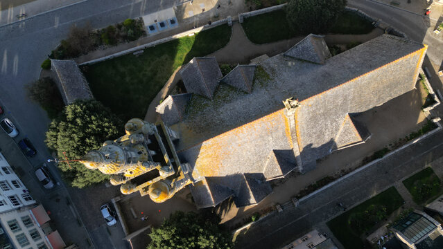 Aerial view of a stone church with a complex roof structure casting long shadows on the surrounding streets, Roscoff, Bretagne, France.