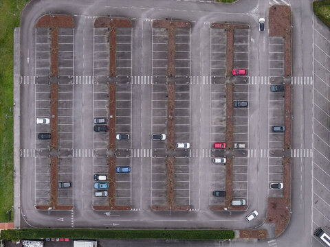 Aerial view of a geometric parking lot with several parked cars and empty spaces surrounded by green grass Leccio, Tuscany, Italy.
