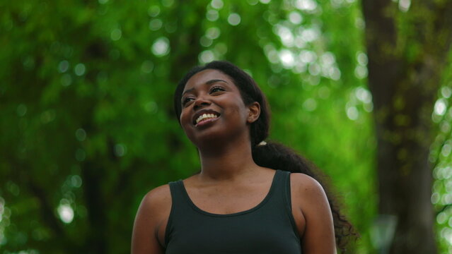 African American woman walking forward with carefree and happy smile while looking ahead as camera tracks her movement creating joyful and uplifting outdoor lifestyle moment in green environment