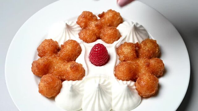 Chef carefully places a vibrant raspberry atop a decadent plate of golden beignets and delicate whipped cream