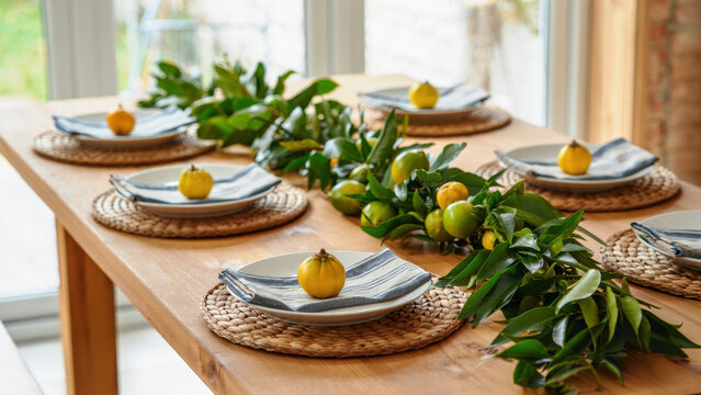 Festive Jewish Sukkot holiday table decoration, citrus etrog fruit green leaf garland decor, wooden dining room interior setting, traditional family dinner preparation, autumn harvest ritual, diy set