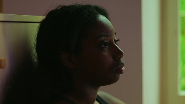 African American woman close up profile by window with distant gaze expressing sadness dissatisfaction and emotional emptiness while feeling lost and aimless indoors