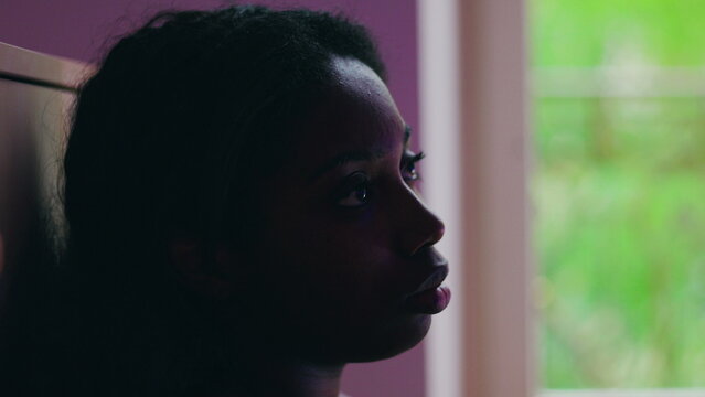 African American woman close up profile by window with distant gaze conveying quiet dissatisfaction introspection and sense of being stuck in unresolved life situation