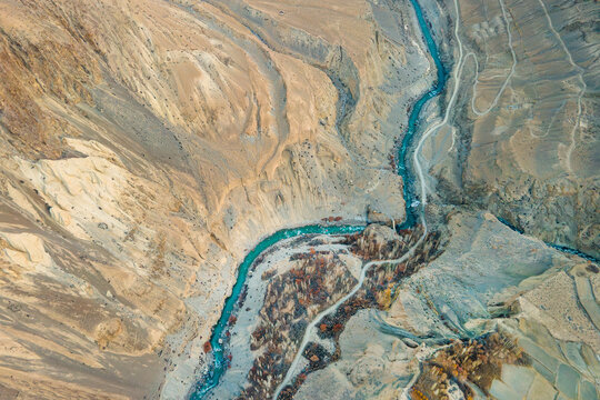 Aerial view of a turquoise river carving through the rugged, textured landscape of Chapursan Valley, creating a mesmerizing contrast of colors and forms, Hunza Nagar, Pakistan.