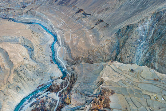Aerial view of the turquoise river snaking through the arid landscape of Chapursan Valley, etched with paths and terraced fields, Hunza Nagar, Gilgit, Pakistan.