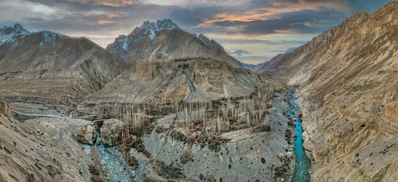 Aerial view of the rugged Chapursan Valley, where the azure river winds through the stark, mountainous terrain under a pastel sky, Hunza Nagar, Gilgit, Pakistan.