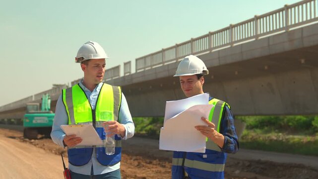 Bridge construction site with engineer team in hard hat and safety vest, inspection and planning with clipboard, blueprint, excavator, and safety helmet workers outdoors for SEO searchability