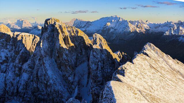 Aerial view of jagged, snow-dusted peaks pierce the skyline, catching the golden light of dawn, Sassopiatto and Sassolungo mountains, Trentino-South Tyrol, Italy.