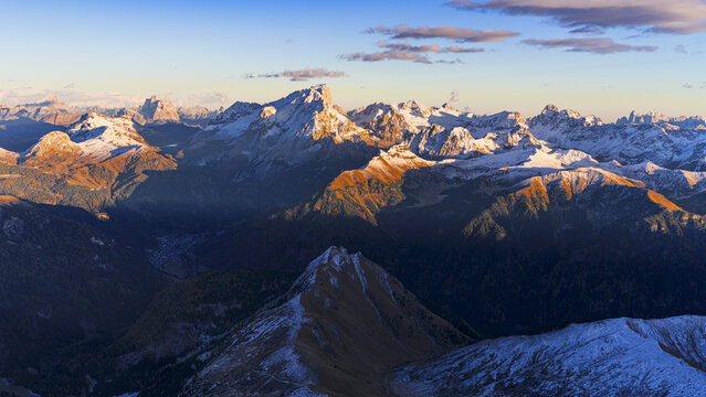 Aerial view of sunlit snow-capped peaks and shadowed valleys create a dramatic tapestry of light and dark across the mountainous landscape, Dolomites, Italy.