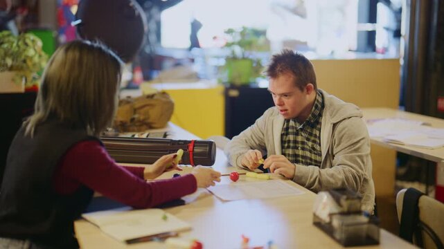 A young man with Down Syndrome and a female student collaborate on a learning exercise. They are actively engaged in an educational activity at a table.