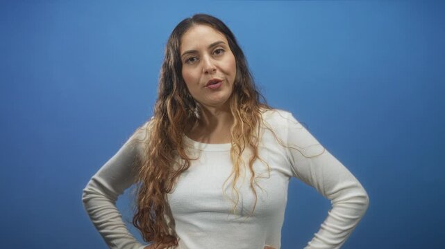 Woman speaking and gesturing with hands in studio blue wall, wearing white sweater and long brunette hair; uncertainty explanation.