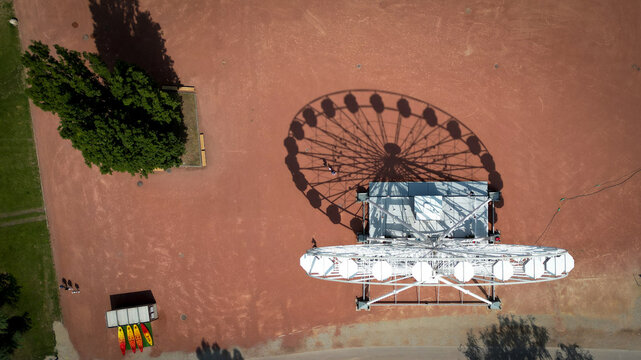 Aerial view of a carousel casting a geometric shadow on the reddish-brown ground near verdant trees, creating a striking contrast of shapes and colors, Neuchatel, Neuchatel, Switzerland.