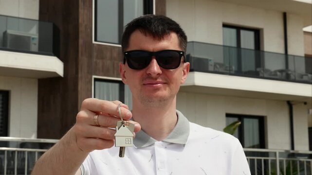 Man holding keys to new home, successful real estate purchase and property investment.
