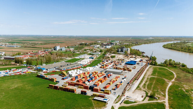 Aerial view of the industrial port area with colorful containers contrasting against the green fields and the winding river Sava, Sremska Mitrovica, Vojvodina, Serbia.