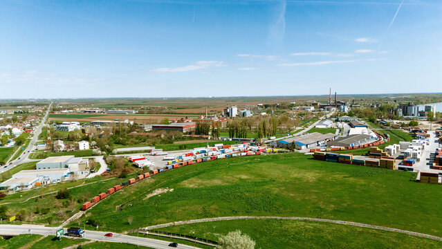 Aerial view of a sprawling industrial landscape, with rows of colorful containers and railcars contrasting against the vibrant green fields, Sremska Mitrovica, Vojvodina, Serbia.