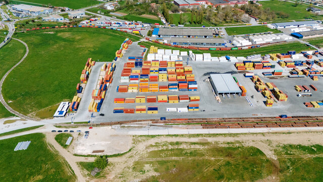 Aerial view of a vibrant container yard with stacked colorful containers contrasting against the green fields, and a network of railway lines, Sremska Mitrovica, Vojvodina, Serbia.