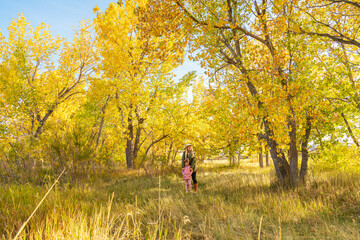 Fototapeta premium Mother Holding Daughter in Sunlit Aspen Forest with Golden Autumn Leaves
