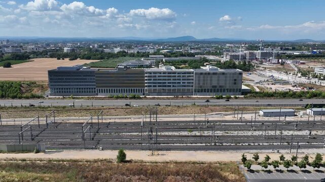 Aerial view of Montpellier France with large modern Flexo building extensive railway tracks and golden harvested fields under bright blue sky