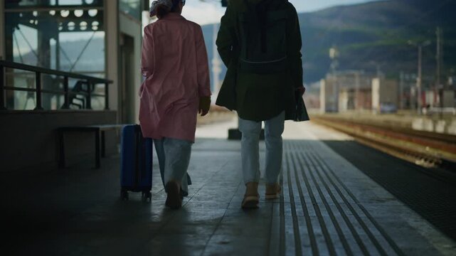 Two tourists with luggage walk along a train platform in a city, preparing for their journey. The couple of travelers stops at the urban train station, ready to embark on an adventure.