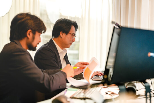 Professional Asian machine learning specialist mentoring a developer on secure coding. Multiethnic corporate experts evaluating privacy preserving AI protocols with paperwork.