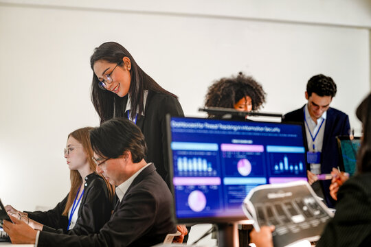 Diverse corporate engineers collaborating on privacy preserving AI. Asian female machine learning specialist helping coworker with secure coding behind blurred foreground monitor.