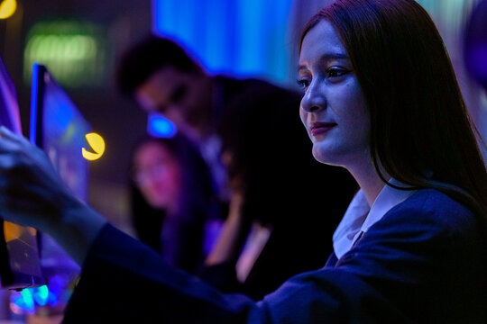 Modern women in technology evaluating big data dashboards and predictive analytics. Tech expert monitoring privacy preserving AI models and autonomous systems with neon lights.