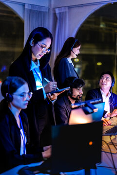 Professional IT support team working in a high-tech command center at night. Focused female specialist using a digital tablet to monitor system status and network security in a neon office.