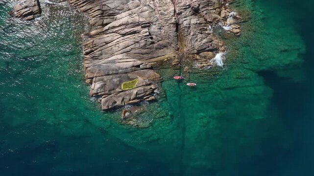 Aerial view of Costa Brava Spain with dramatic layered rocky cliffs clear turquoise water and two paddleboards near the shore under bright sunlight