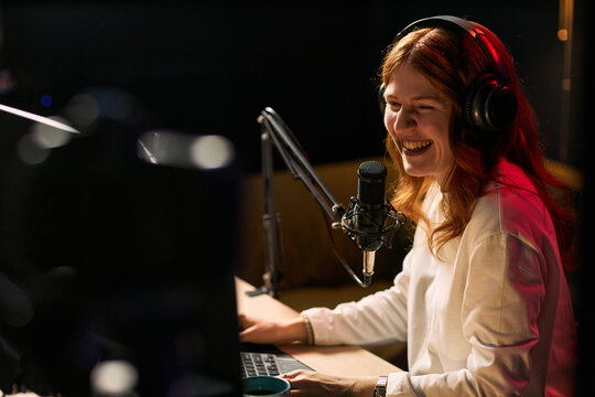 Young adult Caucasian woman streaming content while speaking into microphone and using laptop, representing creator economy and live broadcasting. Ideal for podcast, blogger, social media marketing