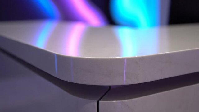 Close up view of a white curved countertop with colorful lights reflecting on its glossy surface