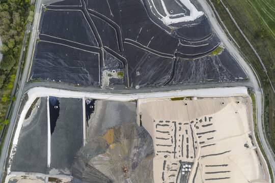 Aerial view of an industrial waste management site with large black and tan protective liners and excavation areas in Pomarance, Tuscany, Italy.
