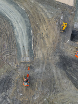 Aerial view of heavy machinery including an excavator and bulldozer working on a construction site with tire tracks on the dirt ground in Pomarance, Tuscany, Italy.