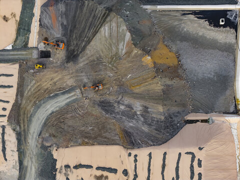 Aerial view of heavy machinery and excavators working on a construction site with dirt mounds and gravel in Pomarance, Tuscany, Italy.