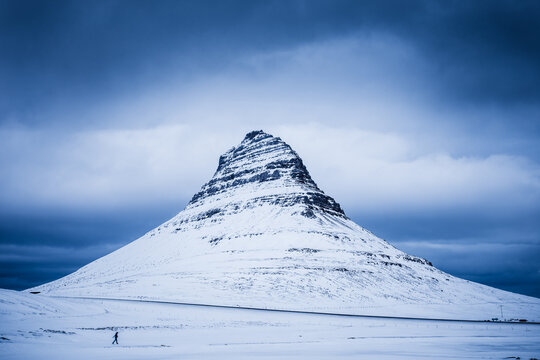 Distant view of a Hiker walking past Kirkjufell mountain on a winter day, Grundarfjordur, Iceland