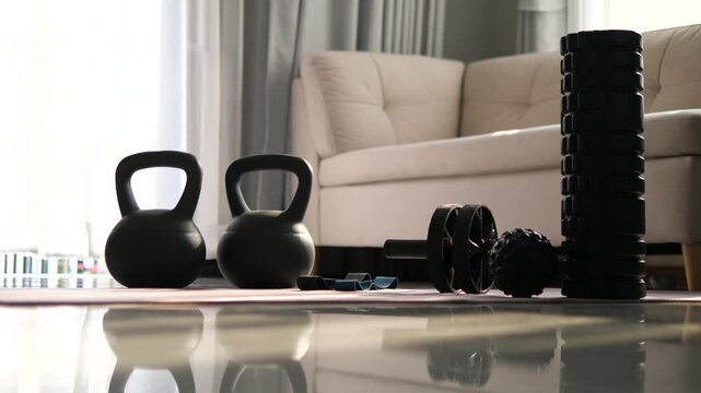 Home workout equipment set including kettlebells, ab roller, and foam roller on yoga mat with morning sunlight shadows for fitness and wellness concept