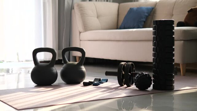 Home workout equipment set including kettlebells, ab roller, and foam roller on yoga mat with morning sunlight shadows for fitness and wellness concept