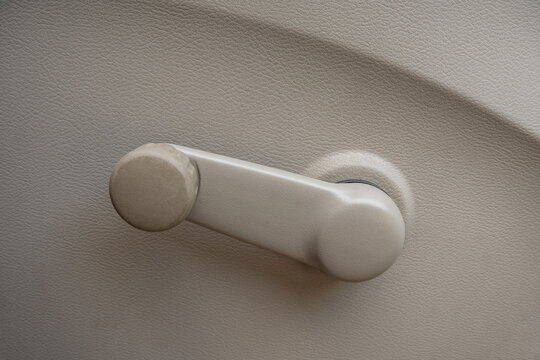Close-up of a manual car window crank handle on a beige interior door panel. Vintage automotive part in a classic or entry-level vehicle.