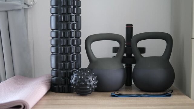 Collection of home workout equipment including kettlebells, foam roller, and massage ball on wooden floor for fitness and recovery concept