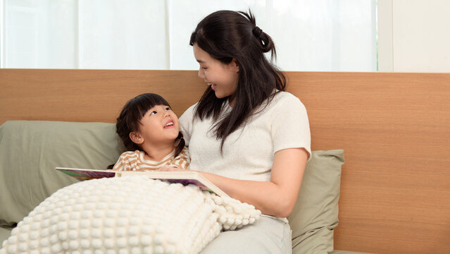 Mother and Child Reading a Book Together in a Bedroom During the Day