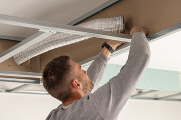 Construction worker handling metal profile frame in suspended ceiling system near flexible air duct