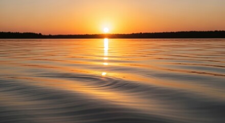 Obraz premium Sunset over calm water with ripples on the surface reflecting the vibrant orange sky