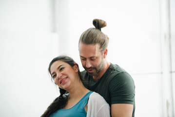 Fototapeta premium Father's Day Concept, affectionate couple embracing indoors with smiling woman and man in casual clothing near bright window