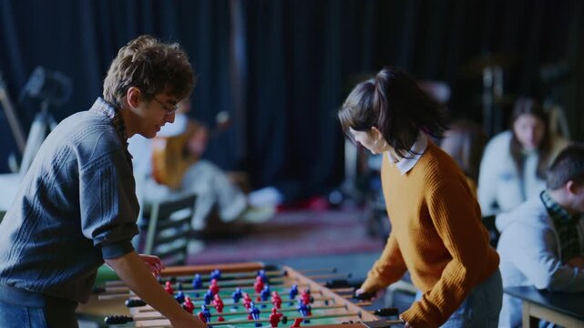 Two happy students enthusiastically play foosball together in a recreational area. They celebrate a goal with a high five, showing friendship and enjoyment.