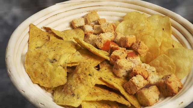 Closeup slow dolly shot of tortilla chip, crisp and crouton snacks, in a white painted rattan cane circular basket, ready to eat.