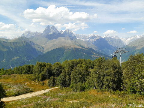 Famous double-peaked mountain Ushba surrounded by green forests under a clear blue sky in the Greater Caucasus mountains, Svaneti, Georgia.