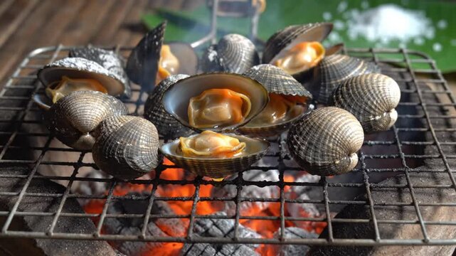 Grilled clams cooking over an open charcoal fire with exposed orange meat and shells sizzling for delicious seafood.