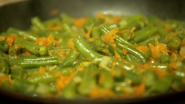 Fresh green beans and shredded carrots are saut ed in a hot frying pan, with steam rising from the vegetables. Concept of healthy eating, home cooking, and vegetarian meal preparation.