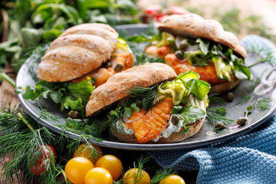 Salmon sandwiches with fresh herbs, zucchini and yogurt sauce on a ceramic plate, focus on a first sandwich in the middle, close up view
